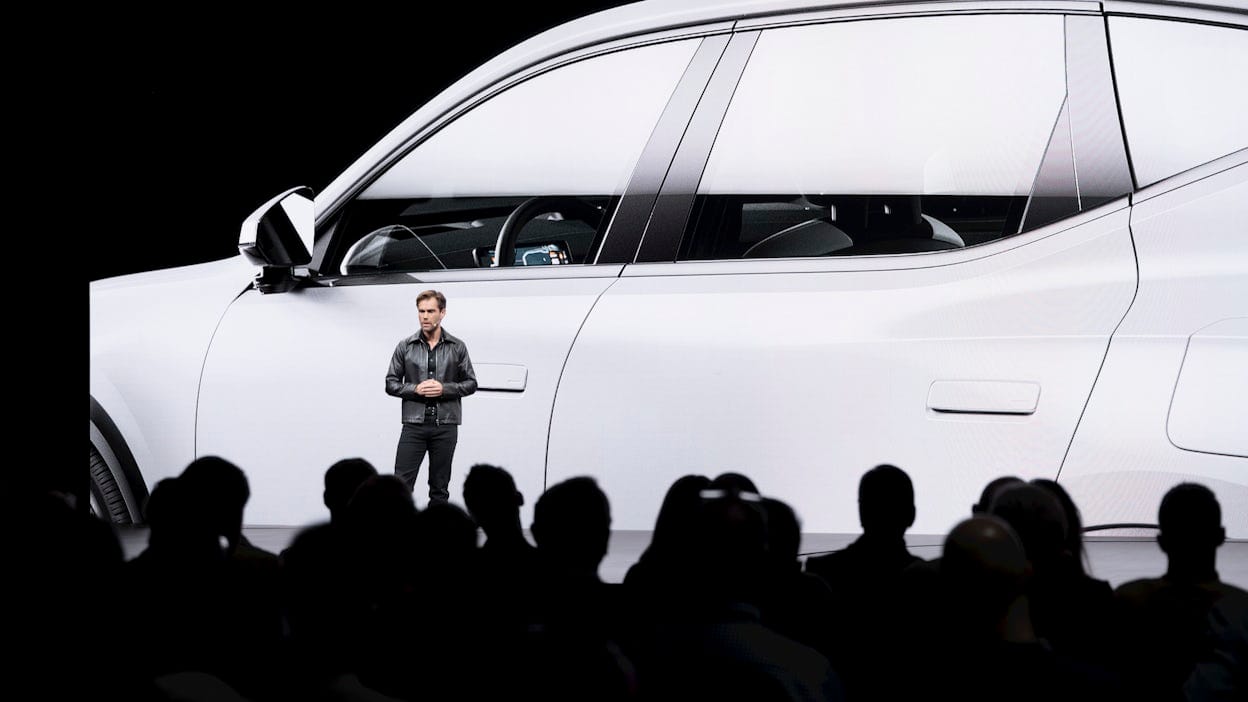 A man standing on stage in front of a screen showing a white Polestar 3.