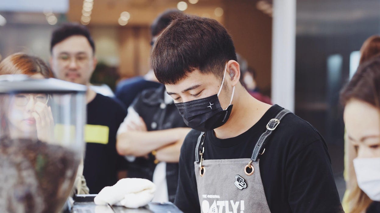 Barista wearing face mask with Polestar logo and apron with the Oatly logo.