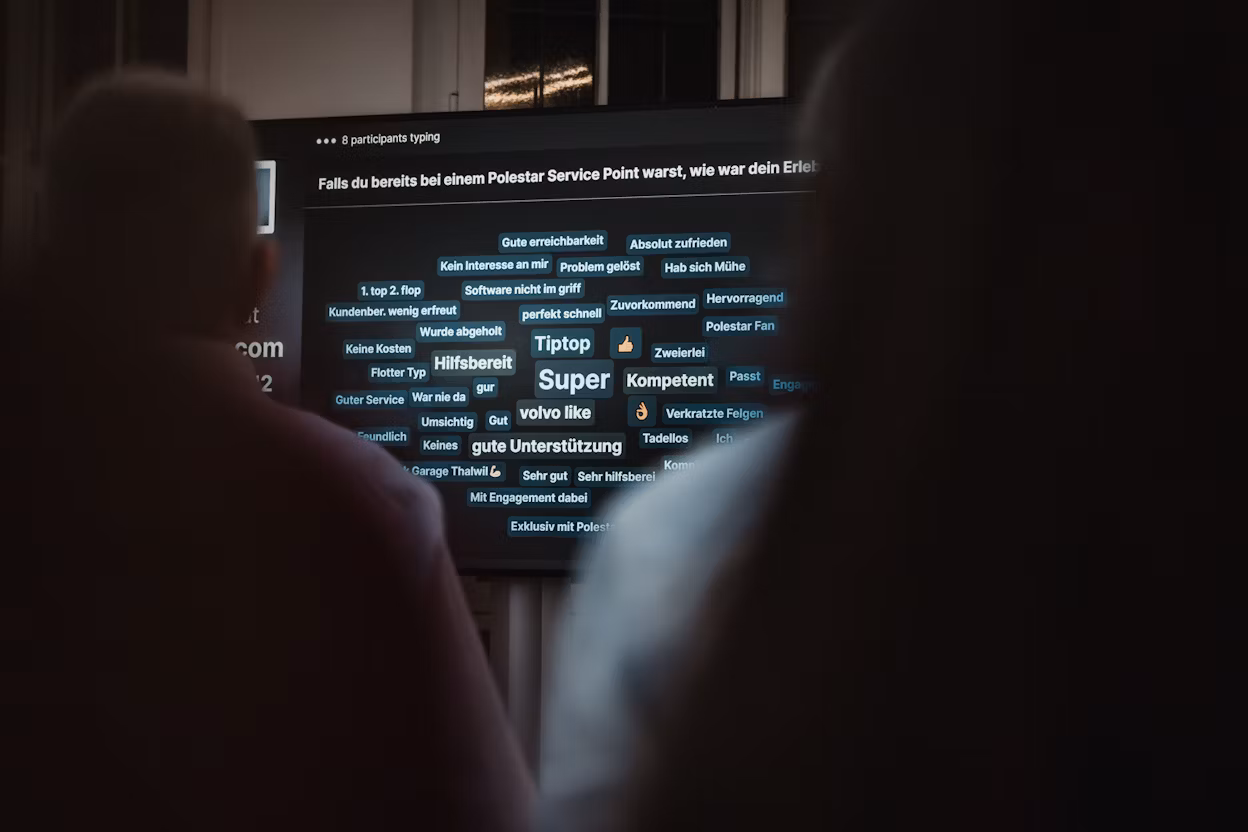 Two people facing a screen displaying feedback about Polestar Service Point with words like 'Super' and 'Hilfsbereit'.