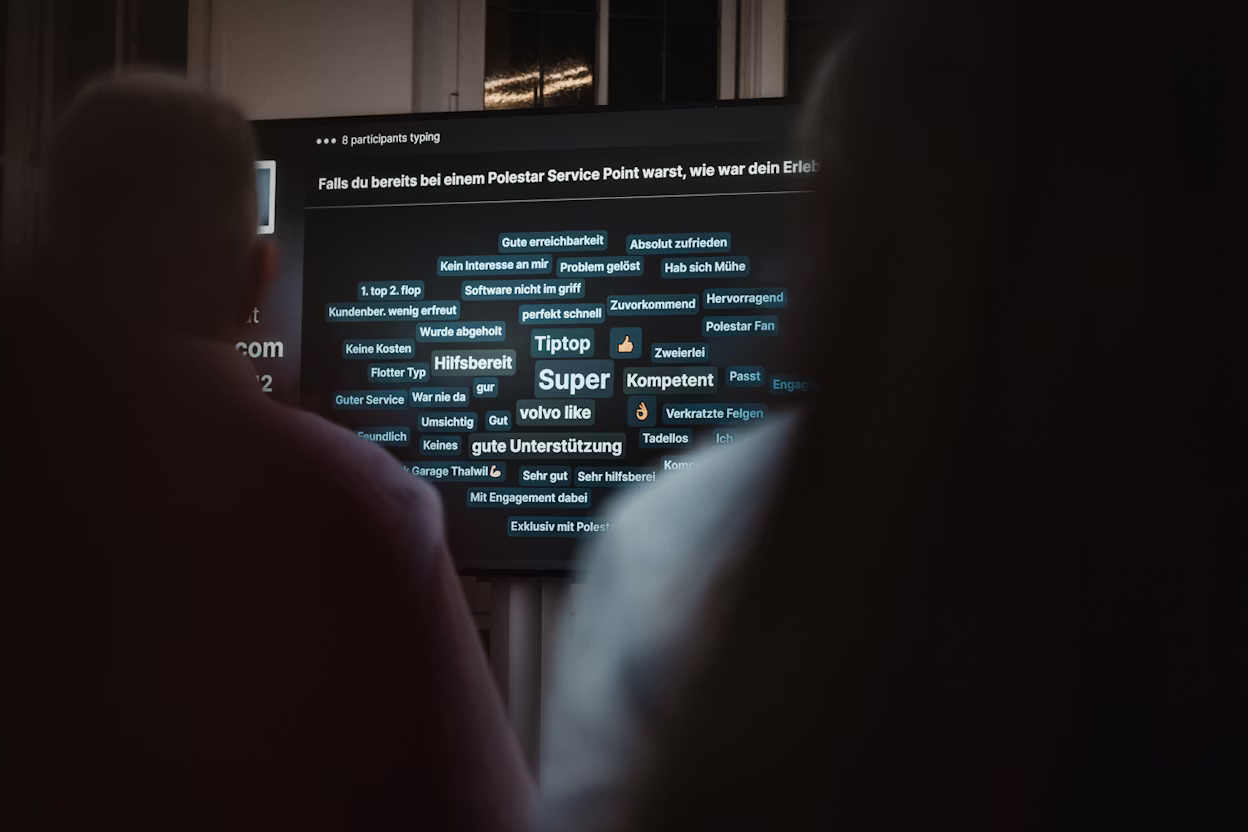 Two people facing a screen displaying feedback about Polestar Service Point with words like 'Super' and 'Hilfsbereit'.