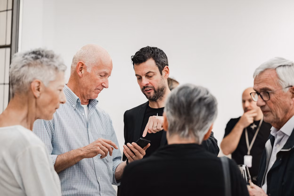 Group of people in conversation indoors, one holding a smartphone.