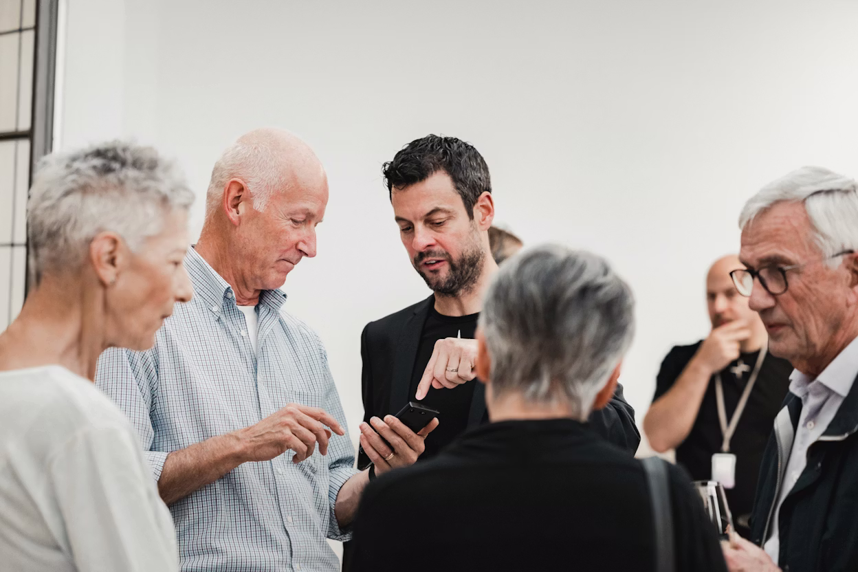 Group of people in conversation indoors, one holding a smartphone.