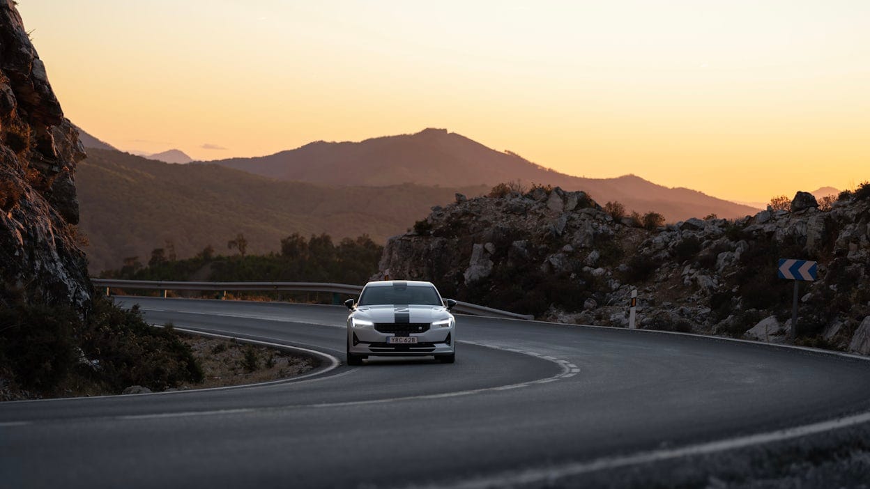 Front view of a Polestar 2 driving on a road at sunset.