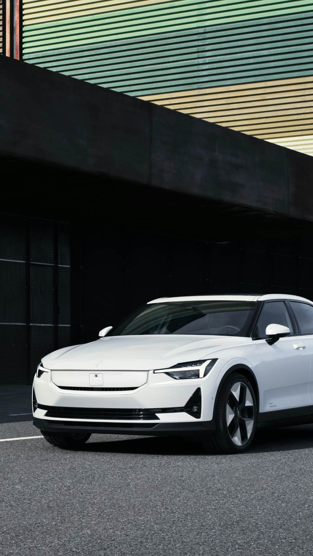 Side view of a white Polestar 2 in motion on a road with industrial background