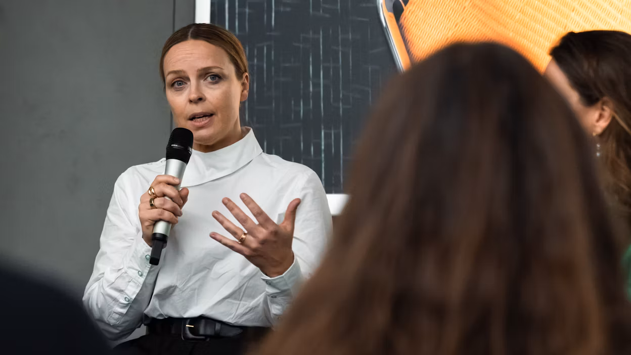 Woman in white blouse talking in a mic in front of a group of people