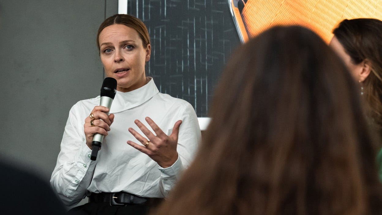Woman in white blouse talking in a mic in front of a group of people