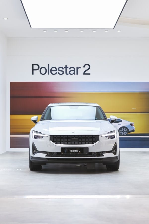 White Polestar 2 seen from the front. Colourful blurry image on the wall behind it.