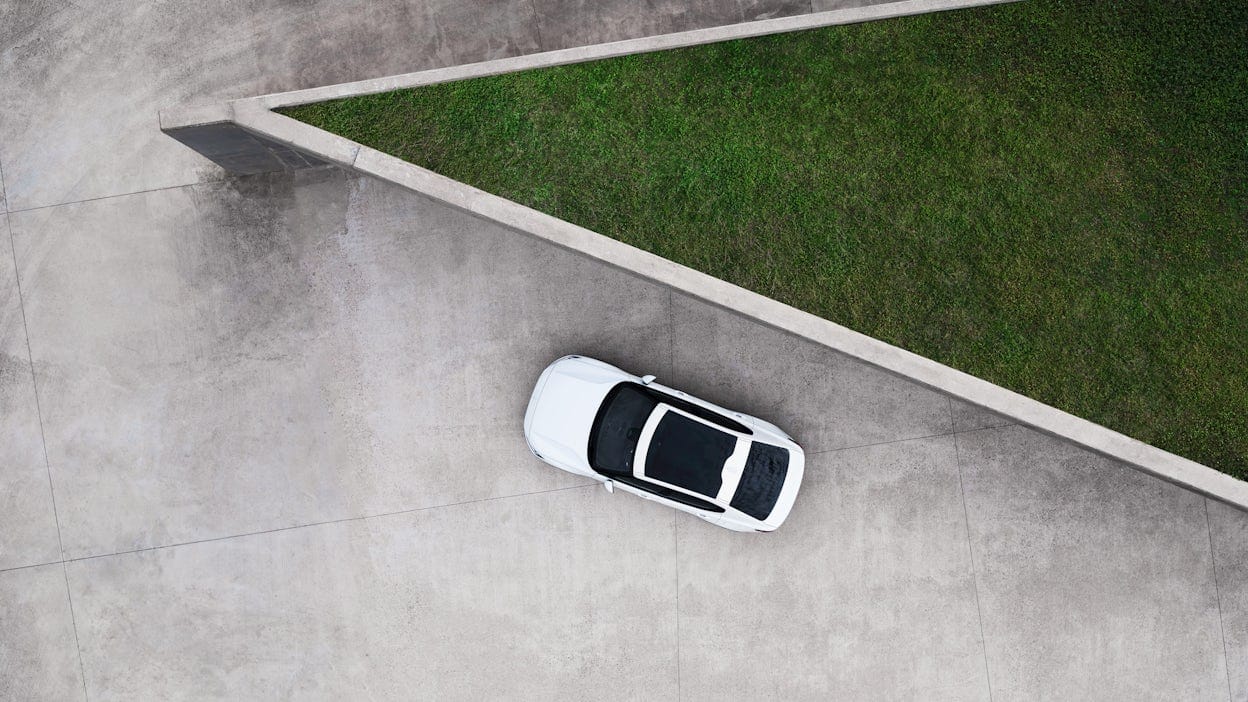 A white Polestar 2 with panoramic roof parked on a concrete platform outside a triangular building with a grass roof.