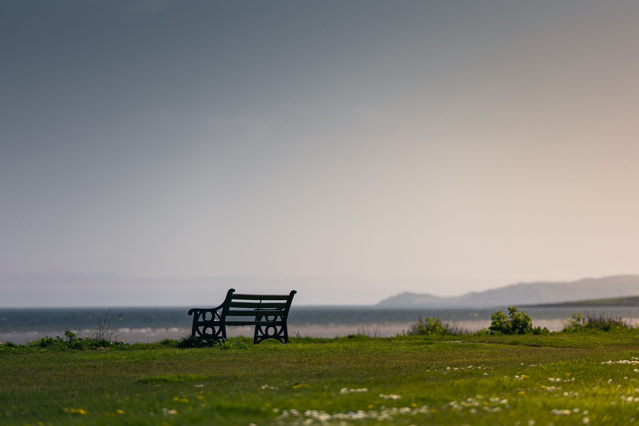 A bench near a charging spot looks out over a beach with green grass in the foreground.