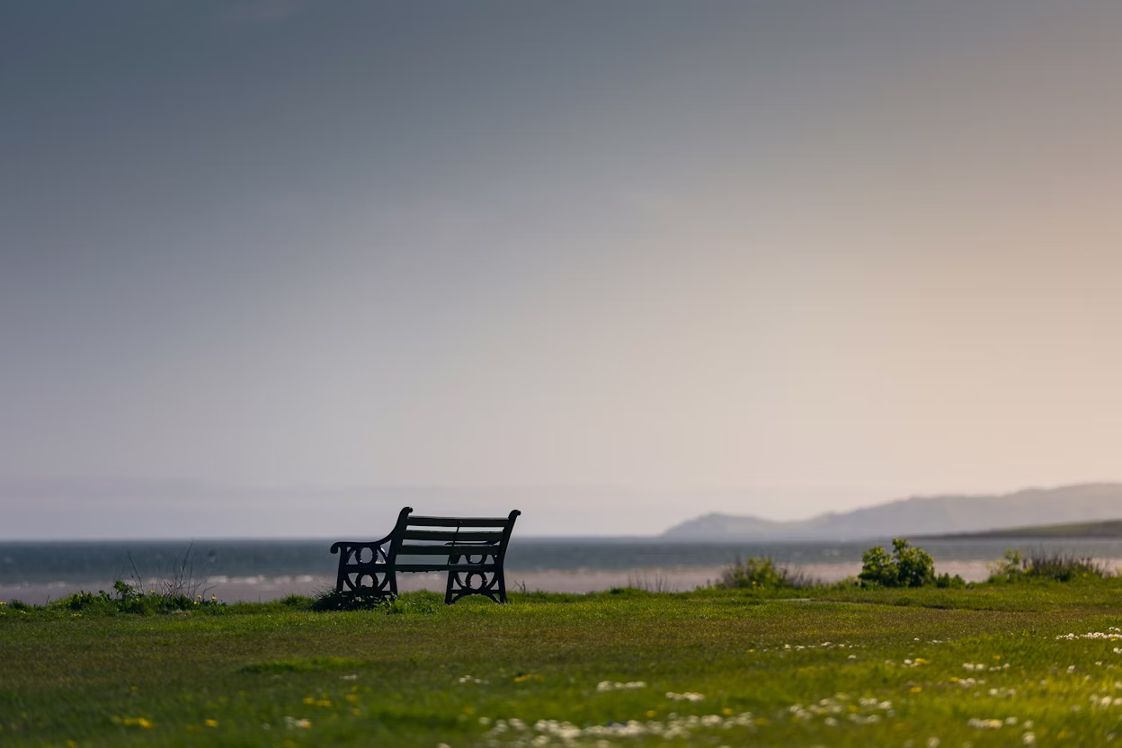 A bench near a charging spot looks out over a beach with green grass in the foreground.
