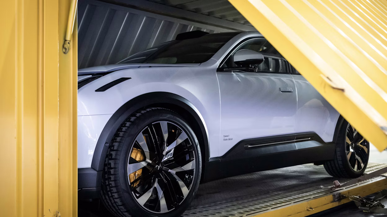 Polestar car inside a yellow shipping container with visible wheels and side mirror.