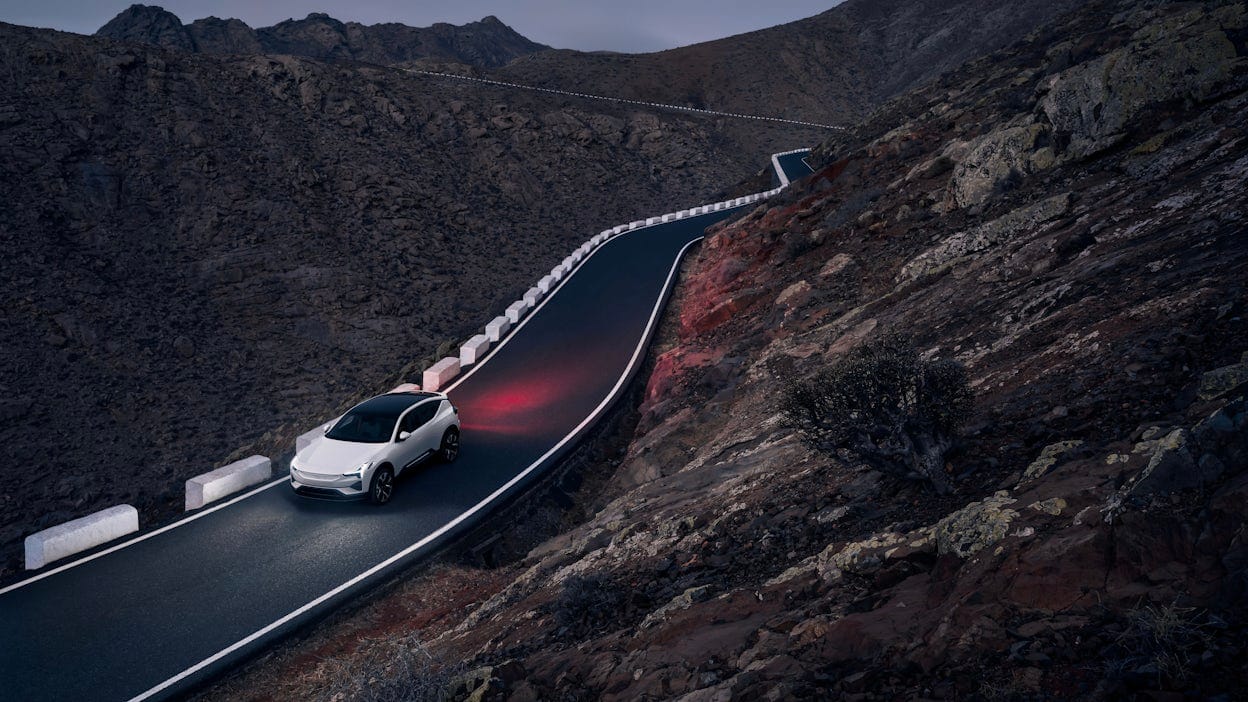 A white Polestar 2 driving on the road between mountains at dusk.