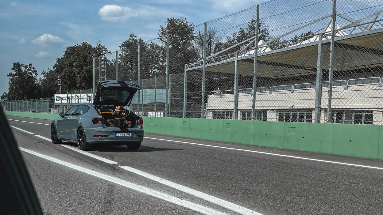 Cameraman waving his hand from the trunk of a Polestar 2 driving on a race track.