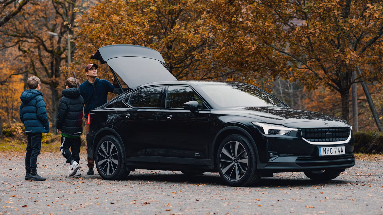 Man and two kids standing next to a black Polestar 2 with an open tailgate.