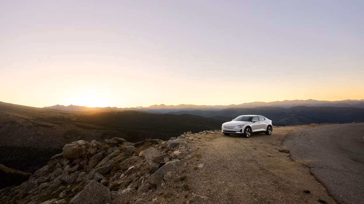 Polestar car parked on a mountain road at sunset with rocky terrain and distant hills visible.