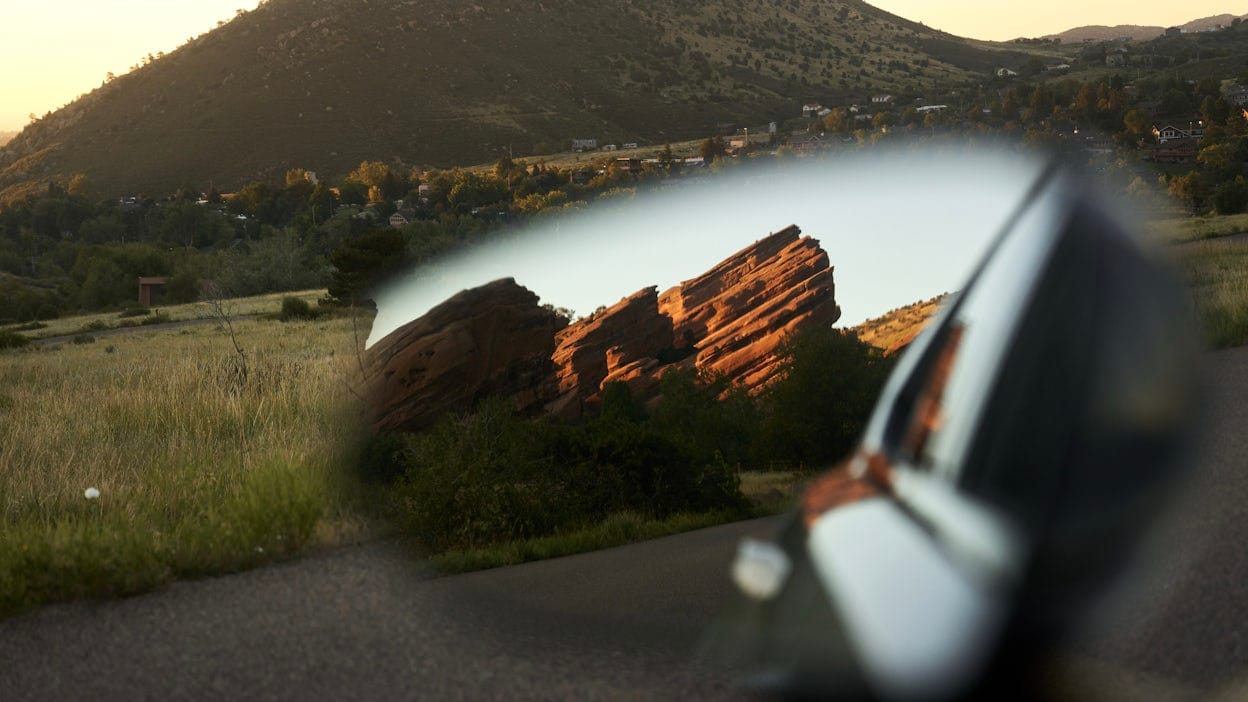Car in beautiful nature with focus on the sun-drenched mountains reflected in the rear-view mirror.