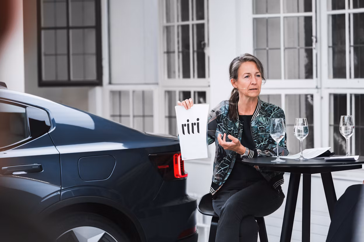 Polestar car parked near a table with glasses and a person holding a paper with 'riri' text.