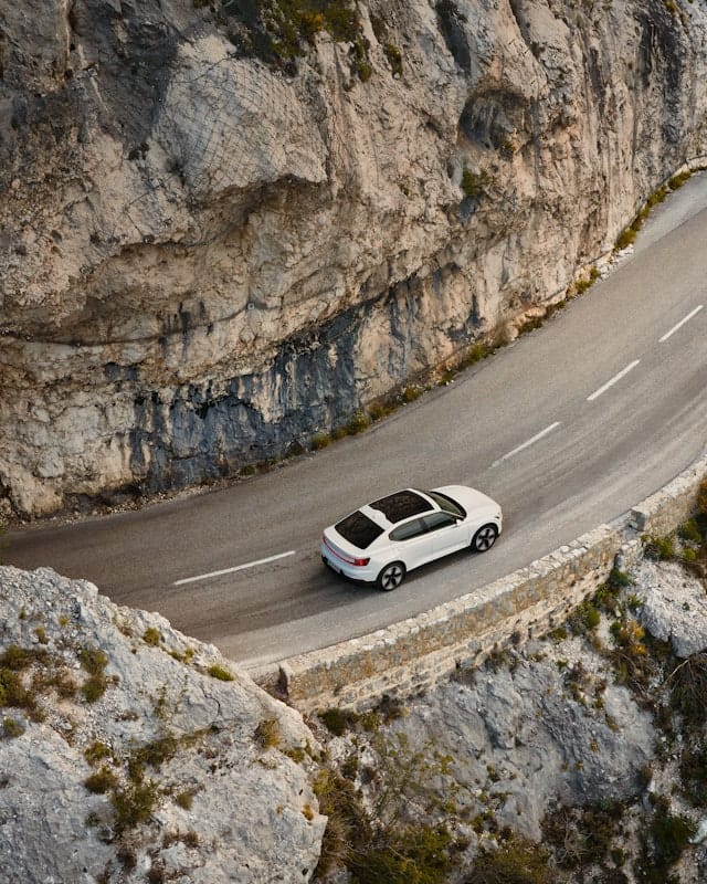 A white Polestar 2 with panoramic roof drivina on a narrow mountain road