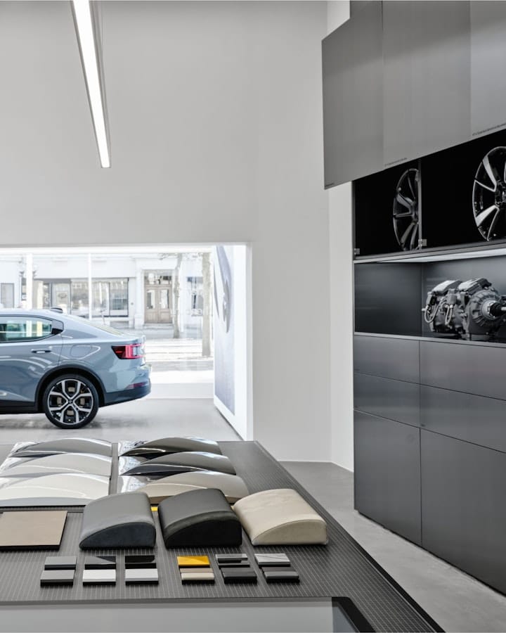 Inside of a Polestar space, showing some interior examples, and the Polestar 2 standing further down the room.
