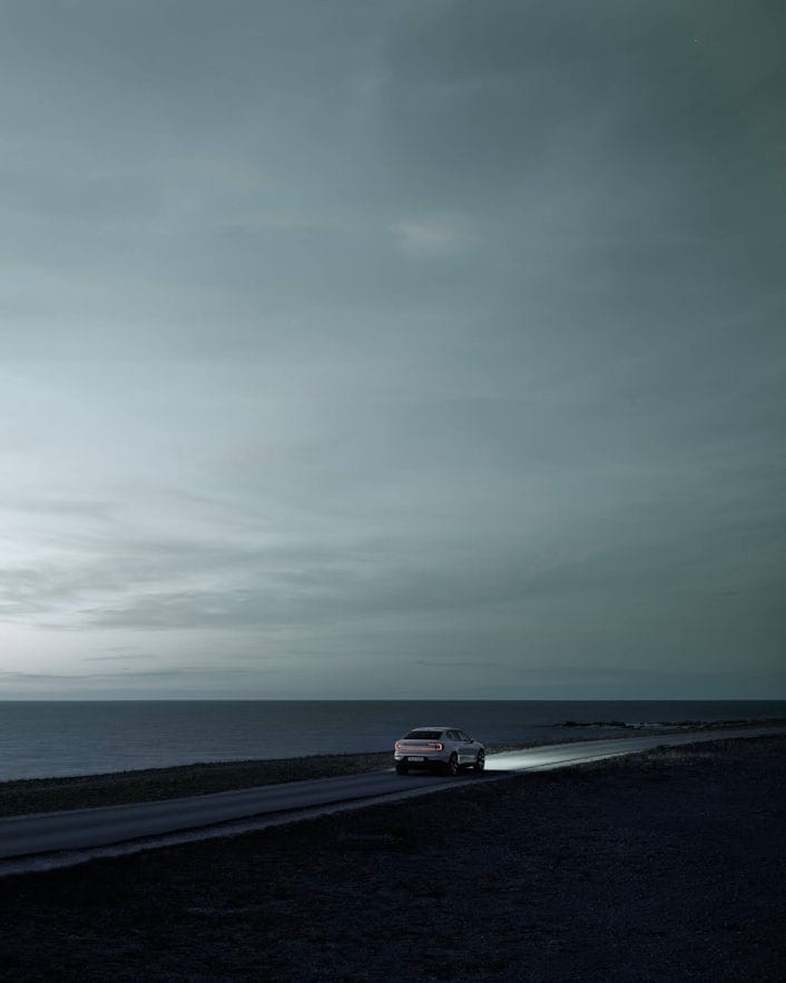 Polestar 2 in distance driving at night next to sea