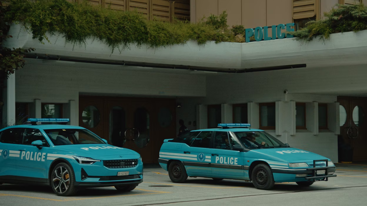 Two police cars, including a Polestar car, parked outside a building with a police sign and greenery on the roof.