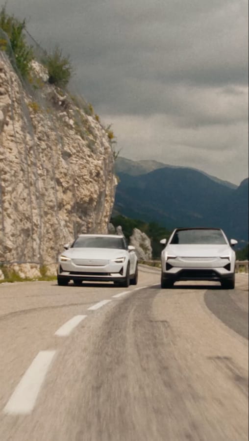 Polestar 2 and Polestar 3 in white driving next to each other down a narrow mountain road