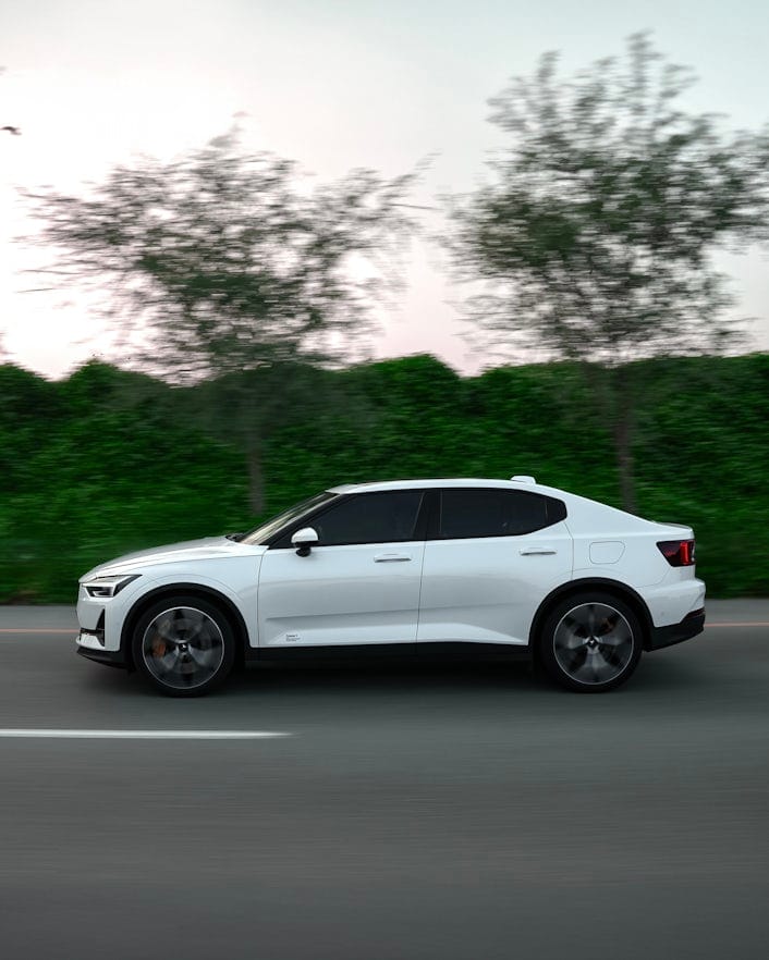 Polestar 2 driving on the road with green trees and bushes behind.