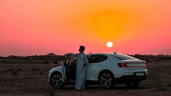 Man leaning on the door of Polestar 2 in the sunset.