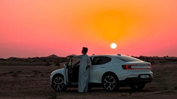 Man leaning on the door of Polestar 2 in the sunset.