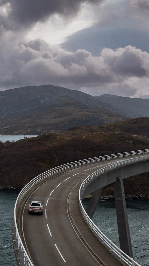 Polestar 2 in white driving across a curved bridge in a scenic Scottish landscape
