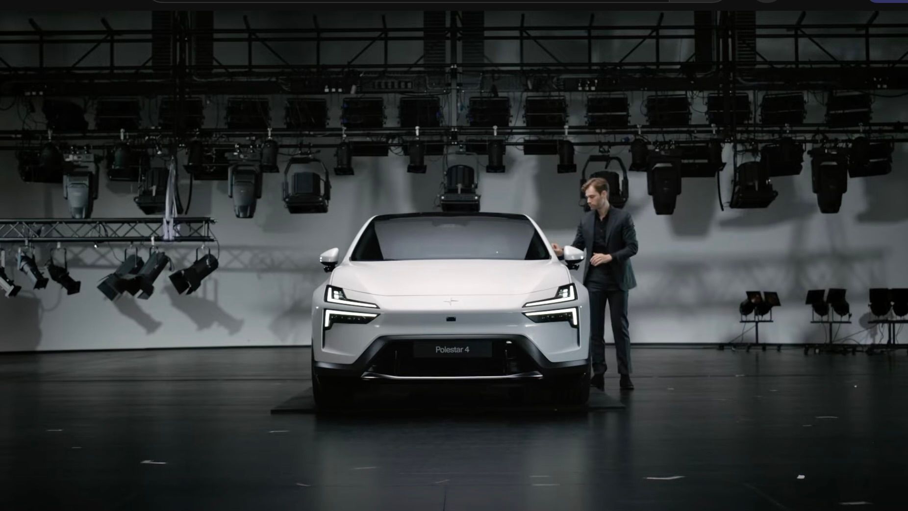 Person standing next to a white Polestar car in a studio with lighting equipment.