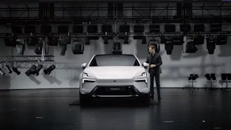 Person standing next to a white Polestar car in a studio with lighting equipment.