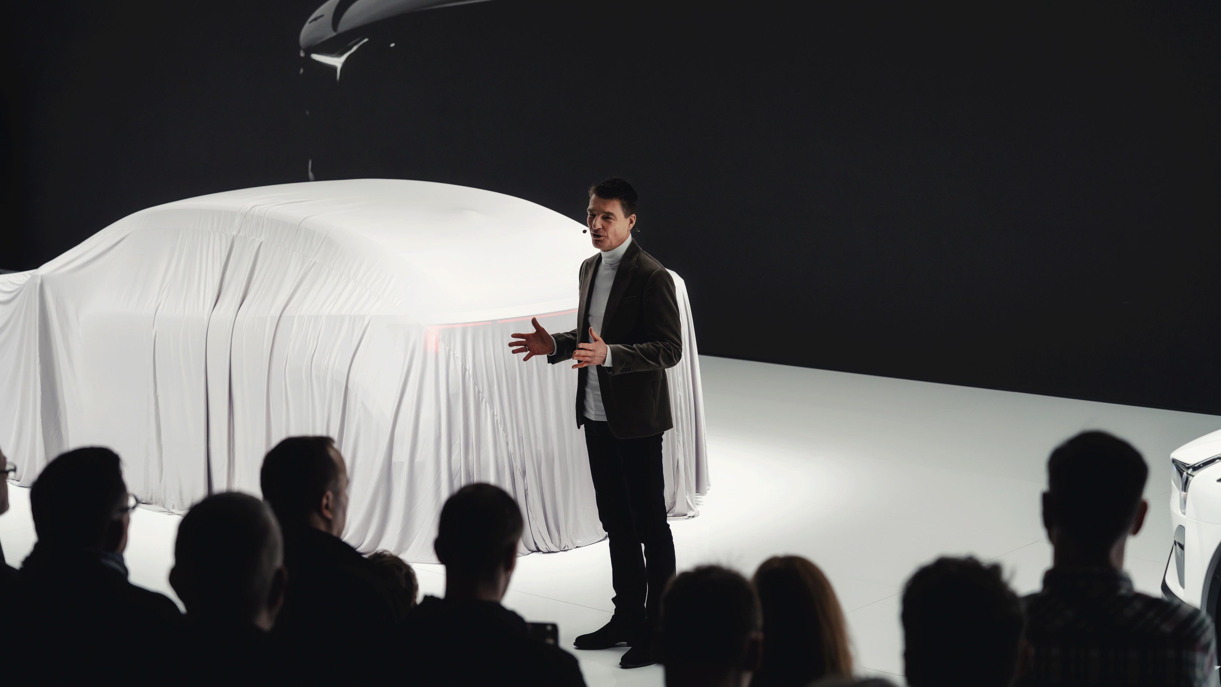 Covered Polestar car on stage with presenter speaking to audience.
