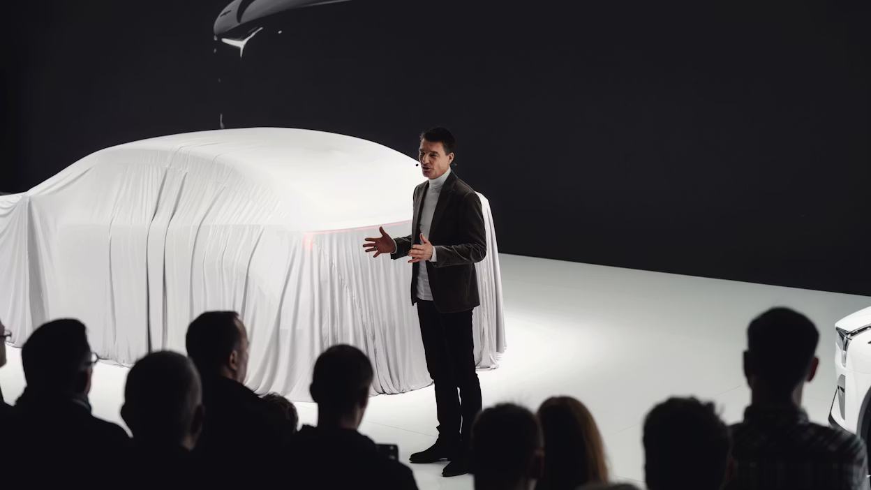 Covered Polestar car on stage with presenter speaking to audience.