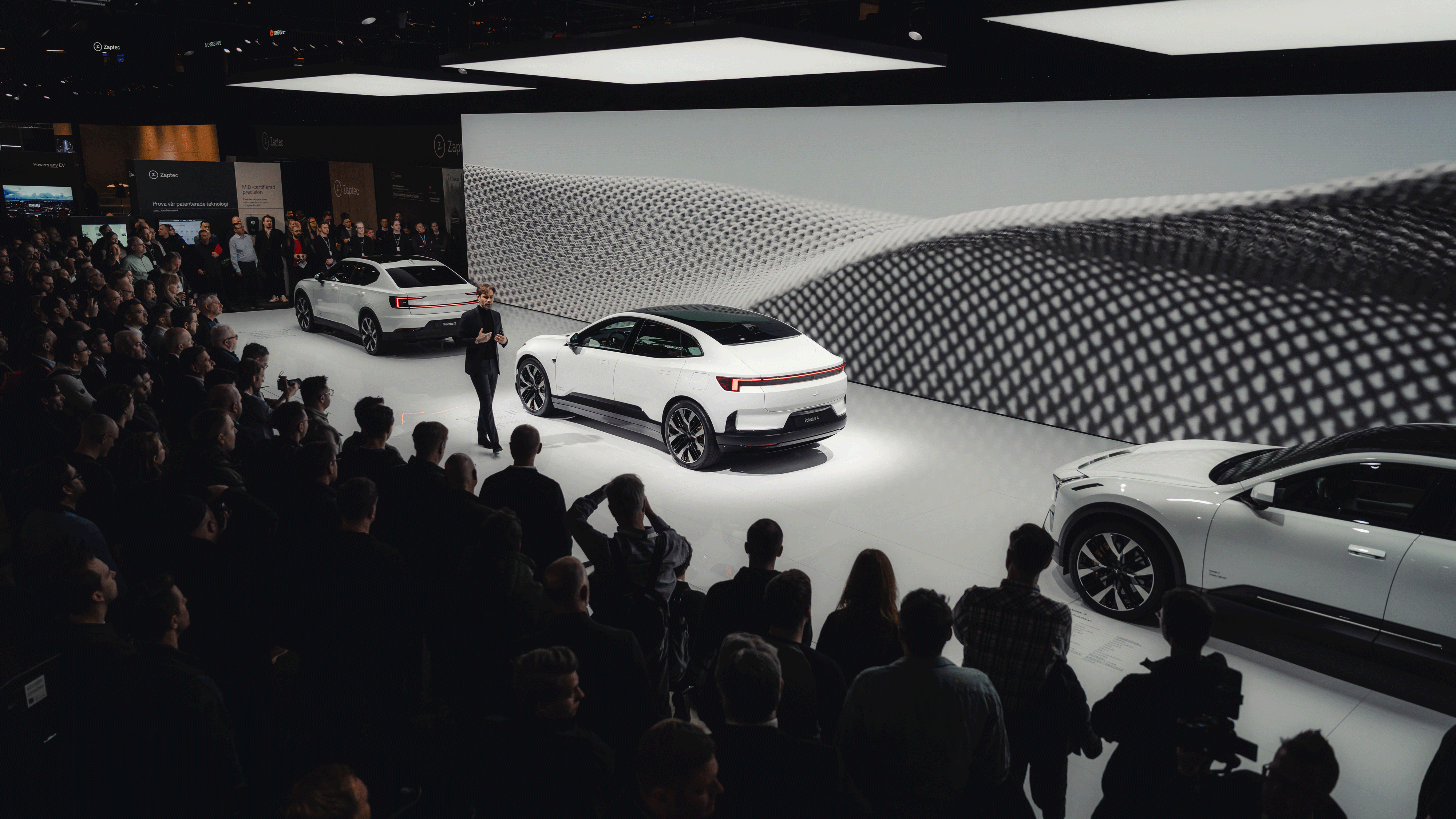 Polestar cars displayed on stage with audience and abstract patterned background.