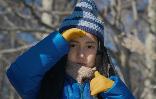Un enfant habillé chaudement avec un manteau bleu et des gants jaunes qui regarde droit dans l'appareil photo.