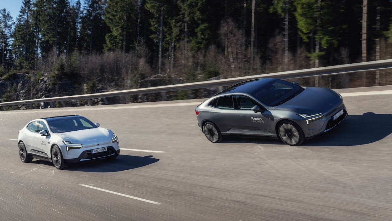 Two Polestar 2 cars driving on an asphalt road, surrounded by forest