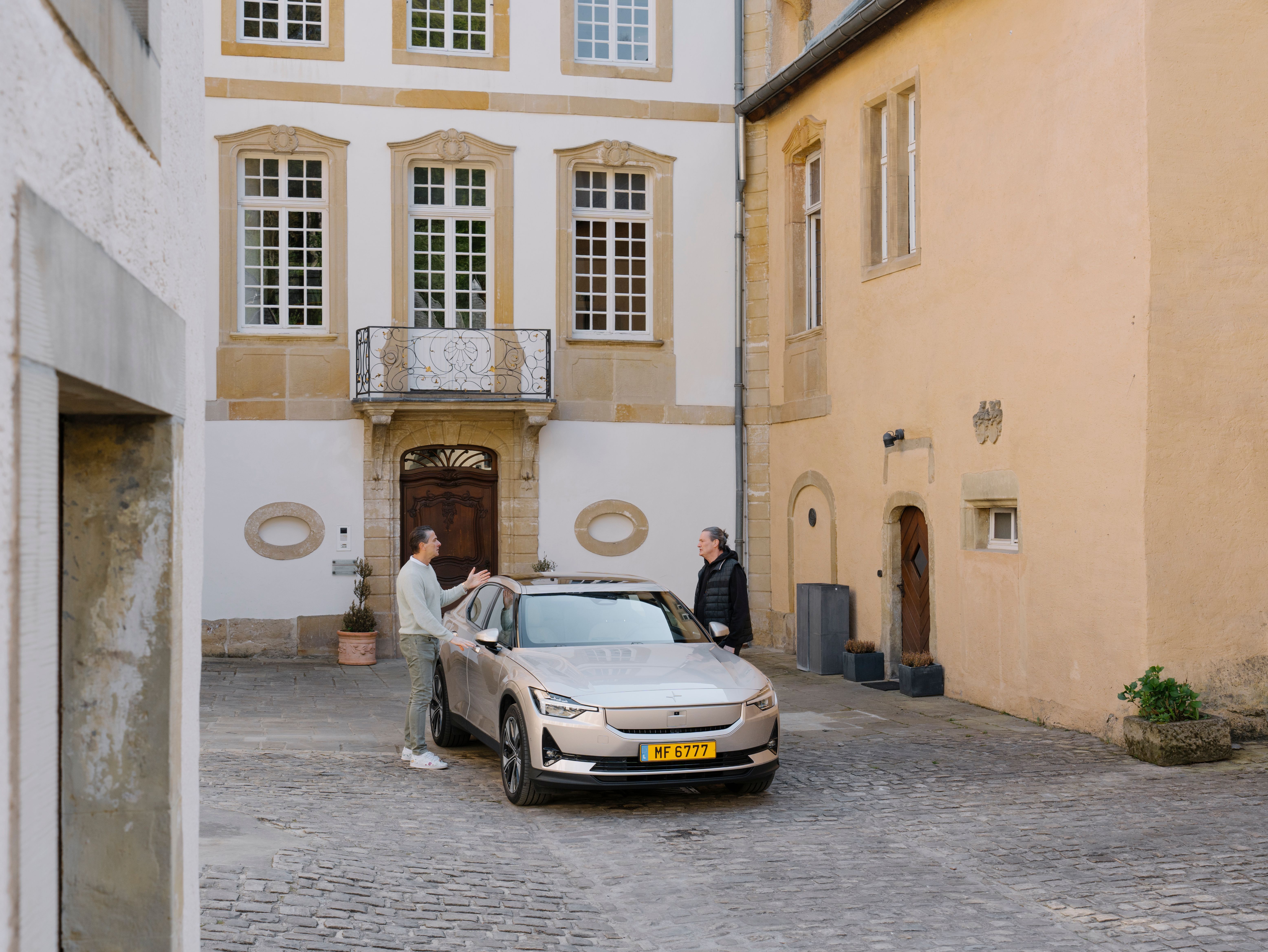 Two people standing near a Polestar car in a courtyard surrounded by historic buildings.
