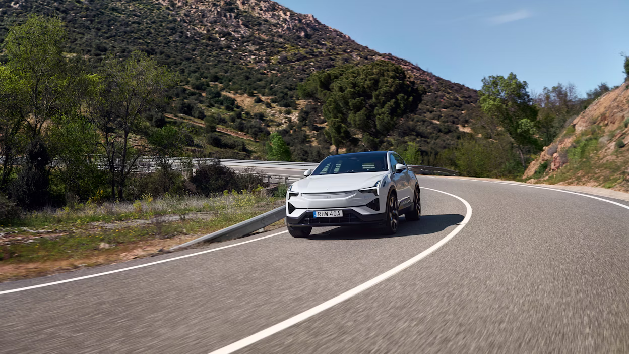 Polestar 3 in Snow color driving on a winding road in Spain, surrounded by trees and mountains