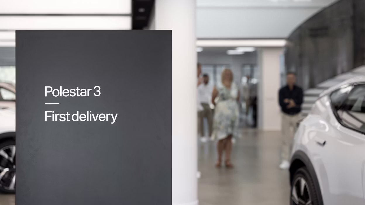 Polestar 3 first delivery sign with a Polestar car and people in a showroom.