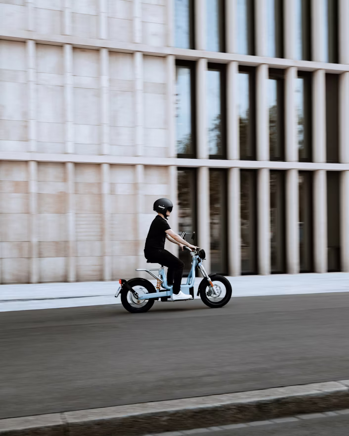 Person riding an electric bike on a street with a modern building in the background.