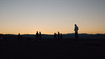 A group of people in the desert at sunset.