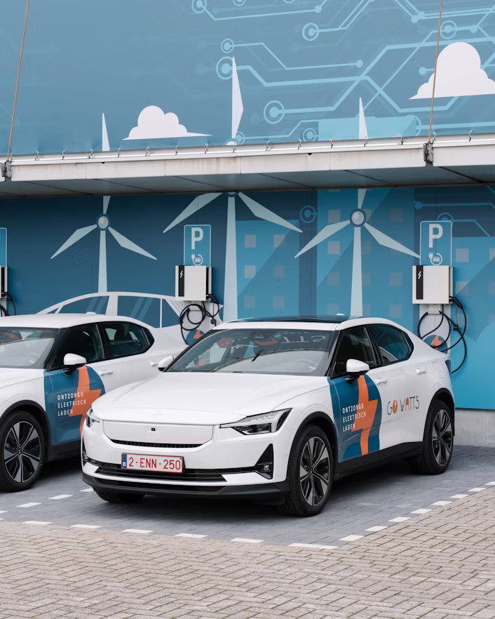 Two Polestar cars parked at electric vehicle charging stations with wind turbine graphics on the wall in the background.