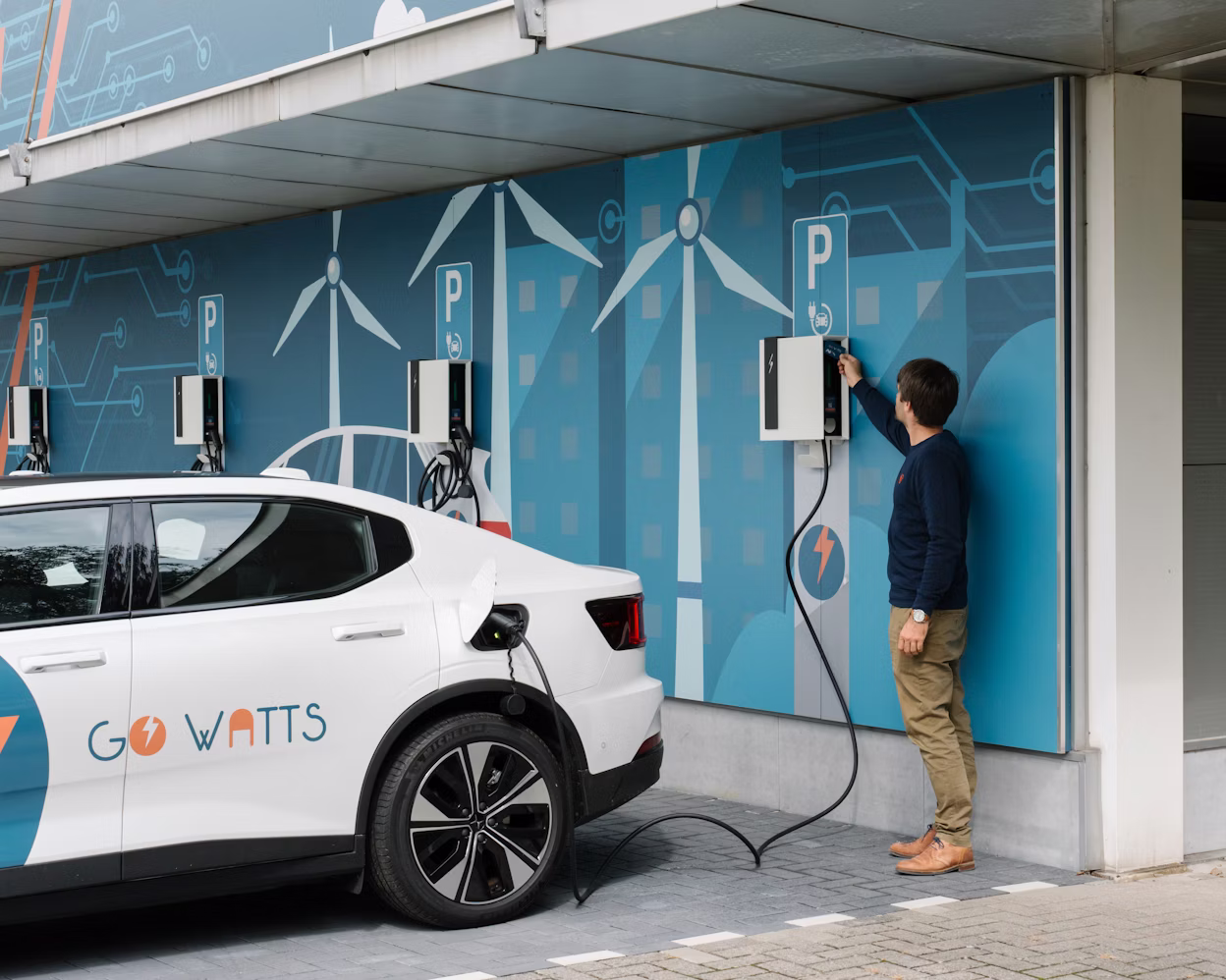 Polestar car charging at a station with a person plugging in the cable, wind turbine graphics on the wall.