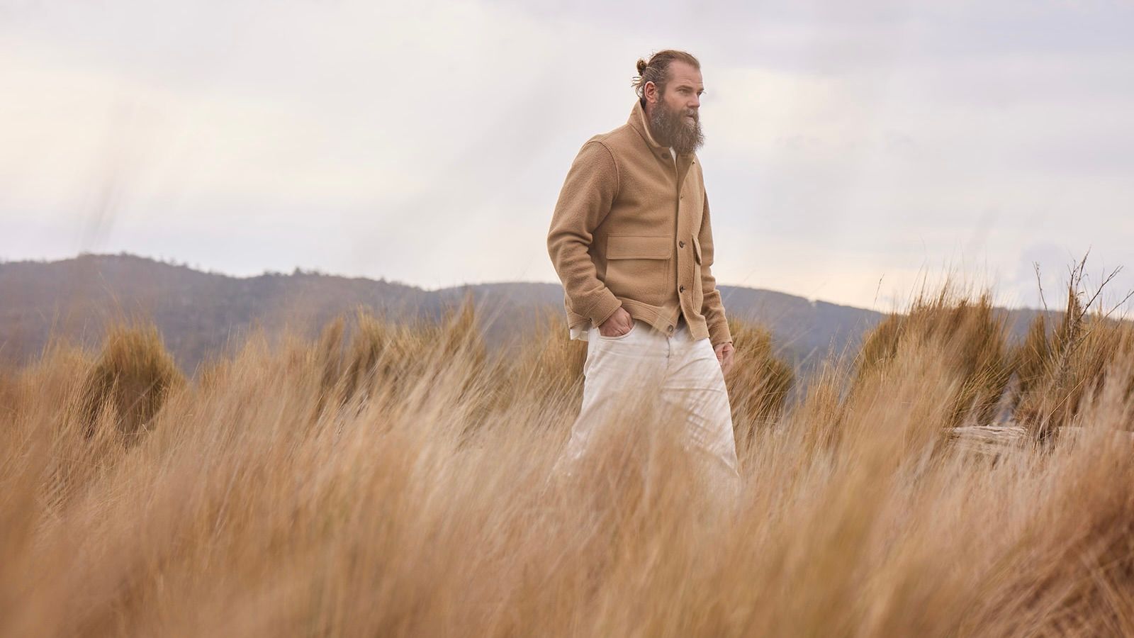 Man walking through tall grass with hills in the background.