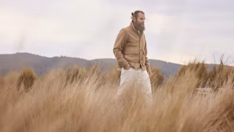 Man walking through tall grass with hills in the background.