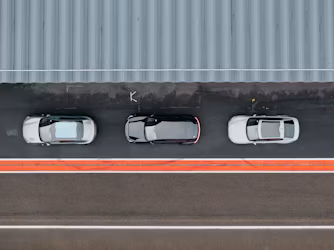 Three Polestar cars parked on asphalt near a corrugated metal wall and red-bordered road.