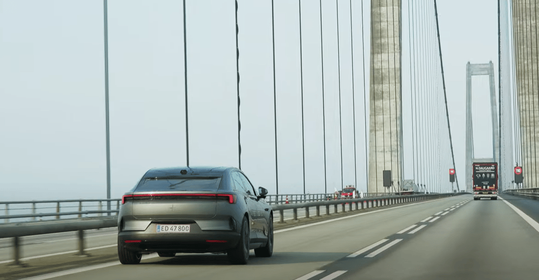 Polestar car driving on a bridge with suspension cables and other vehicles visible in the background.