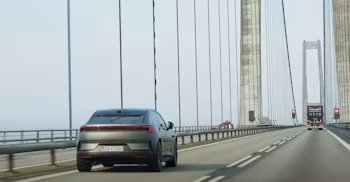 Polestar car driving on a bridge with suspension cables and other vehicles visible in the background.