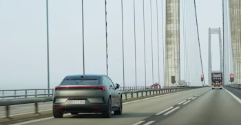 Polestar car driving on a bridge with suspension cables and other vehicles visible in the background.